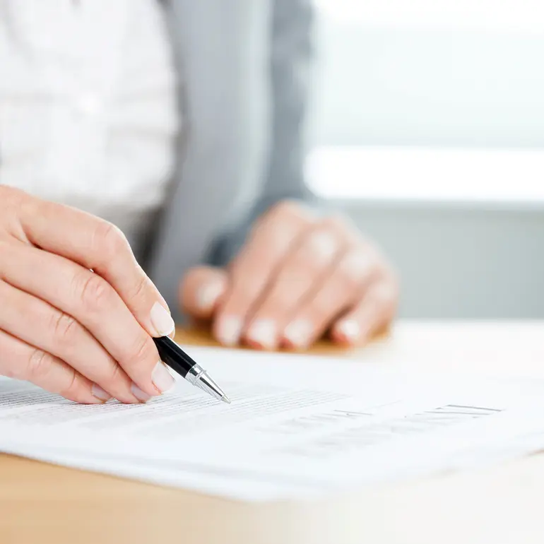 hands holding a pen to paperwork for primary loan servicing on a desk