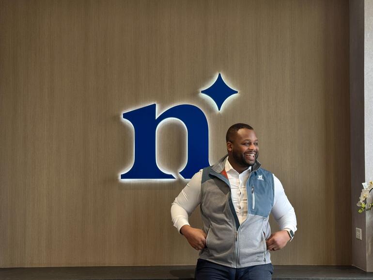 Deon Green, producer at Northmarq, standing in front of a desk with the blue Northmarq logo in the background