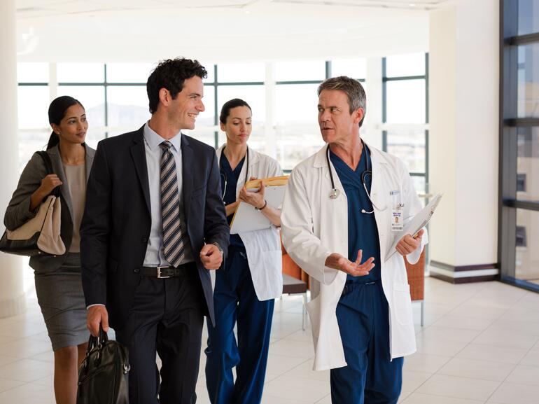 Corporate healthcare operators speaking with advisors and doctors while walking down a hallway
