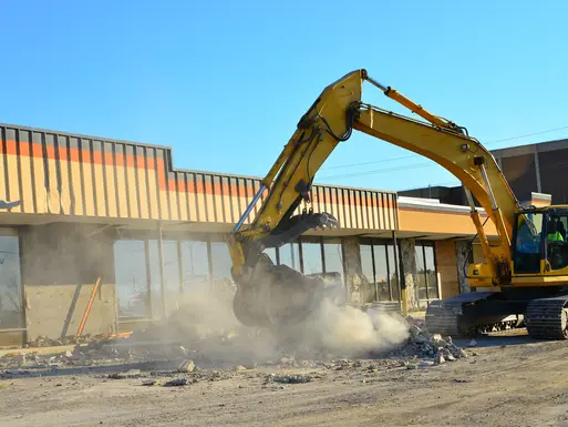 Heavy equipment works to demolish strip mall in urban area