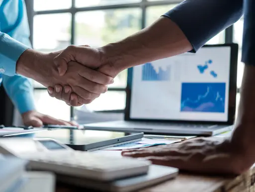 Equity broker shaking hands with commercial real estate investor client with computer screen in the background